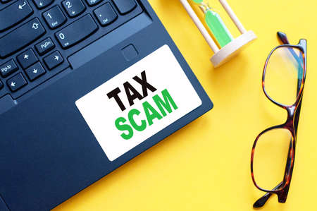 White paper card with text TAX SCAM sheet of white paper for notes, calculator, hourglass, glasses in the white background. Business concept. Yellow background.の写真素材