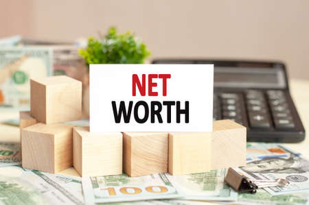White paper card with text NET WORTH on the calculator. Business concept. Brown background.の写真素材