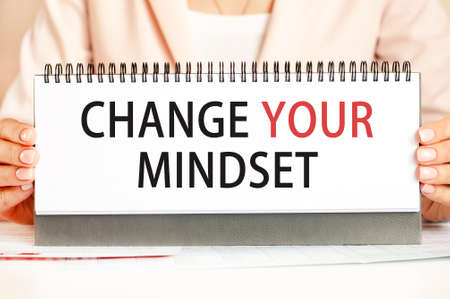 The woman holds a cardboard with hands with the text CHANGE YOUR MINDSET. Text writing black and red letters. Business and economics concept.の写真素材