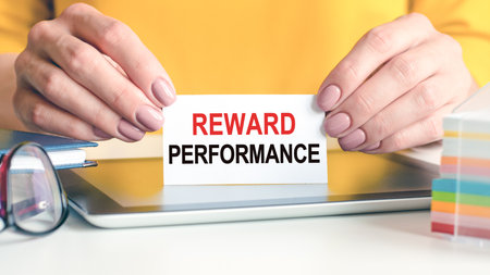 Reward performance is written on a white business card in a woman's hands. Yellow background....