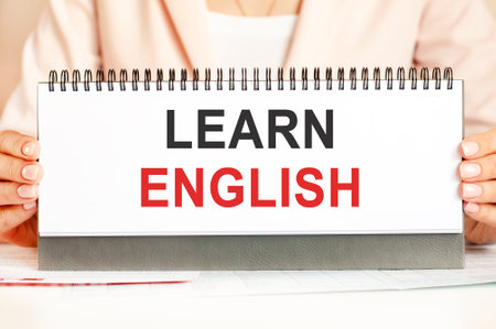 the woman holds a cardboard with hands with the text learn english. Text writing black and red letters. Business, economics, education concept.の写真素材