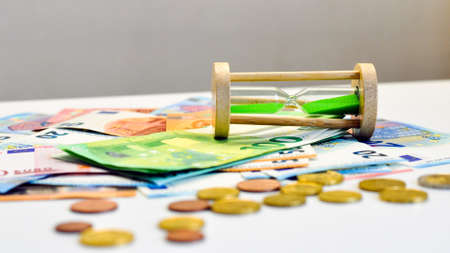 HOURGLASS PAPER MONEY AND COINS ON THE TABLE