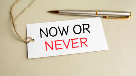 white card with text Now or Never with metal pen on gray backgroundの写真素材