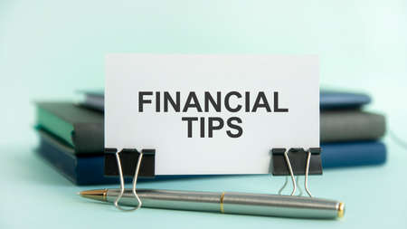 a white card with the text FINANCIAL TIPS stands on a clip for papers on the table against the...