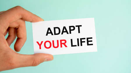 businessman's hand holding paper business card with text ADAPT YOUR LIFE, closeup light blue background, business conceptの写真素材