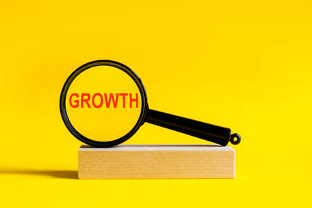 the inscription growth through magnifying glass on yellow background. the magnifying glass is mounted on a wooden stand on a tableの写真素材