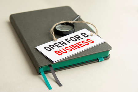 on the gray notebook is a magnifying glass and a white paper card with the inscription open for...