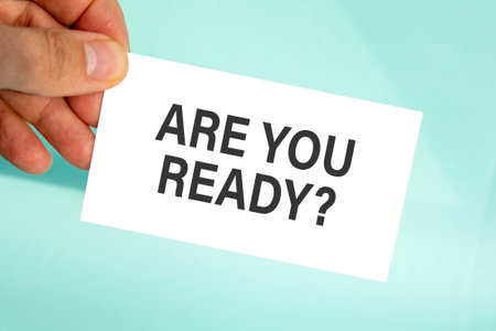 businessman's hand holding paper business card with text are you ready, closeup light blue background, business conceptの写真素材