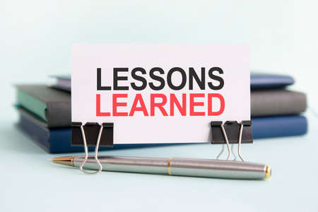 a white card with the text lessons learned stands on a clip for papers on the table against the background of books. selective focusの写真素材