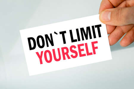 businessman's hand holding paper business card with text dont limit yourself, closeup light gray background, business conceptの写真素材