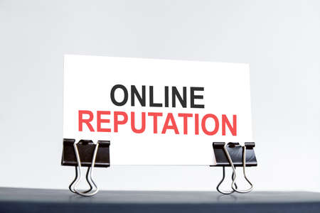 a white card with online reputation text stands on paper clips on a desk against the light blue background. Unfocused.の写真素材