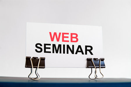 a white card with web seminar text stands on paper clips on a desk against the light blue background. unfocused.の写真素材