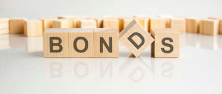 bonds - word of wooden blocks with letters on a gray background. Reflection of the caption on the mirrored surface of the table. Selective focus.の写真素材