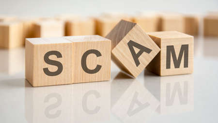 four wooden blocks with the letters scam on the bright surface of a gray table. the inscription on the cubes is reflected from the surface of the table.の写真素材