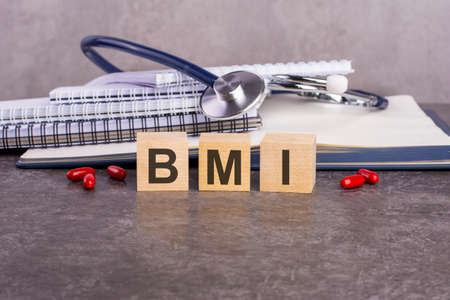 the word BMI is written on wooden cubes near a stethoscope on a paper background. medical conceptual word collected of wooden elements with the letters. BMI - short for body mass indexの写真素材
