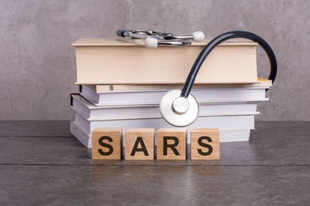 word sars is written on wooden cubes near a stethoscope on a gray background. medical concept for hospital, clinic and medical business. concept of medical education with book and stethoscopeの写真素材