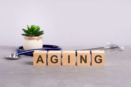 aging word written on wooden blocks and stethoscope on light gray backgroundの写真素材