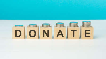 donate text on wooden blocks with coins on blue background, business conceptの写真素材