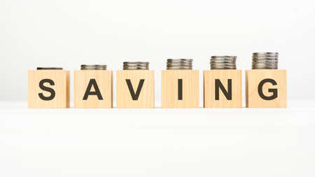 saving text written on wooden block with stacked coins on white background, business concept