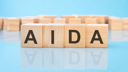 word AIDA on wooden cubes on blue background. business concept for salary or payment for the job done. AIDA - short for Attention Interest Desire Actionの写真素材