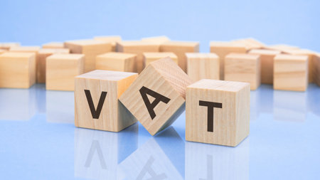 three wooden cubes with the letters VAT on the bright surface of a pale lilac table. the inscription on the cubes is reflected from the surface of the table, blur background. financial conceptの写真素材