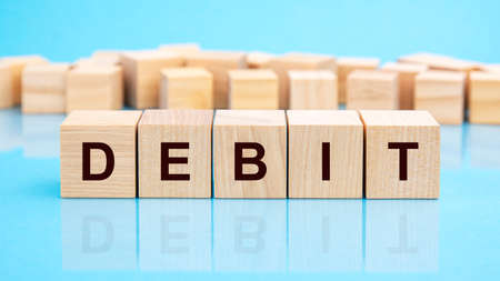 four wooden blocks with the letters Debit on the bright surface of a blue table. the inscription on...