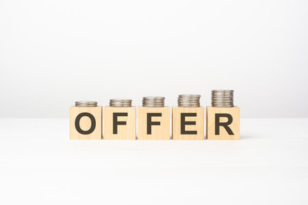 offer text written on wooden block with stacked coins on white background, business conceptの写真素材