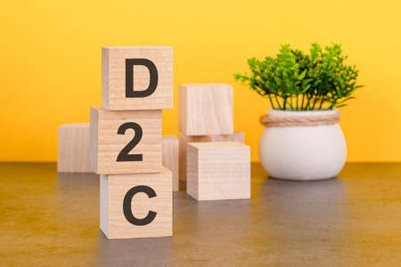 Three wooden cubes with letters - D2C on yellow table, space for text in right. front view concepts, flower in the background. D2C - short for Direct to Consumerの写真素材