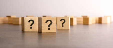 three wooden blocks with question marks with focus to the single cube in the foreground in a...