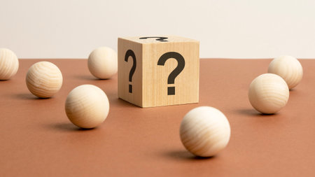 wooden cube with question sings surrounded by wooden spheres on a brown table backgroundの写真素材