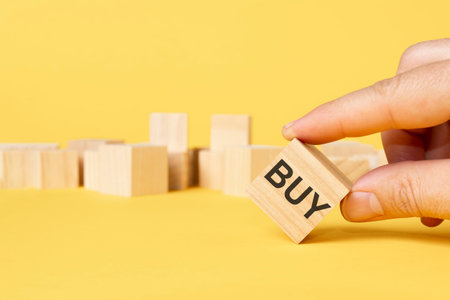 man hand chosen wooden block with word BUY on yellow backgroundの写真素材