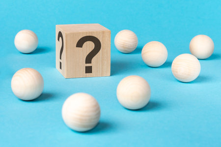 wooden cube with question sings, surrounded by wooden spheres on a blue table