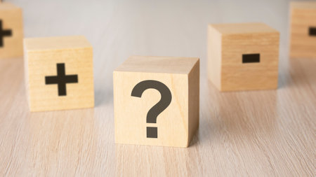 plus minus sign on the faces of a wooden cube. many wood cubes with question marks on light backgrondの写真素材