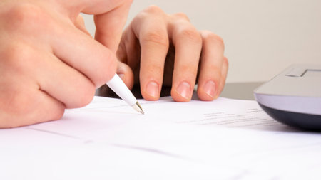 close shot of a human hand writing something on the paper. on the foreground magnifier glass,...