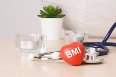 the word bmi is written on red heart shaped toy on on wooden table near a stethoscope on background.の写真素材