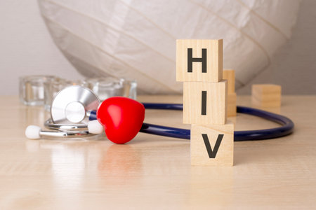 the word hiv is written on wooden cubes near a stethoscope, red heart shaped toy on wooden table background.の写真素材