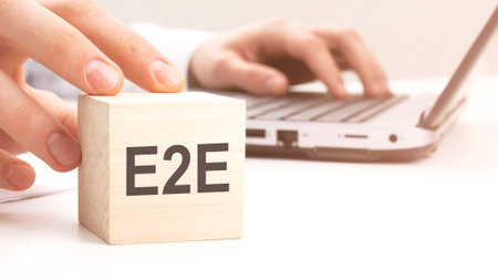 man holding wooden cube witt letters E2E in the background a laptop on a white office table backgroundの写真素材