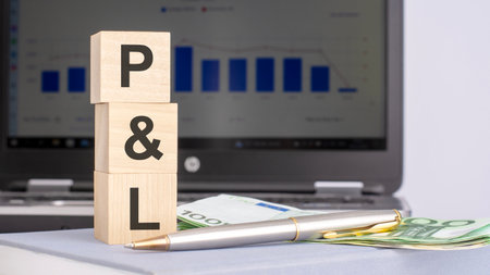 close-up of wooden blocks with the acronym P and L and banknotes on the background of a laptop, business conceptの写真素材
