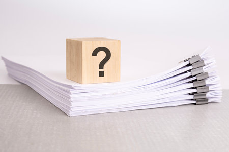 a wooden cube with a question mark on a stack of documents. grey table, white backgroundの写真素材