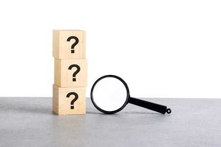 three question sign on wooden blocks with magnifying glass on gray tableの写真素材