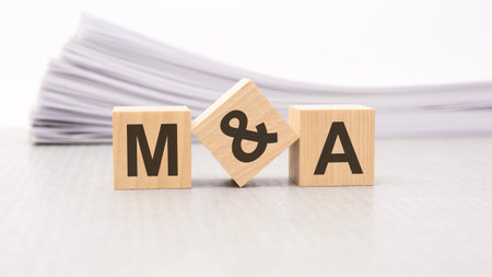 wooden cube with text M and A - acronym - Mergers and Acquisitions . wooden cubes are on the paper white background, business concept. front view.の写真素材