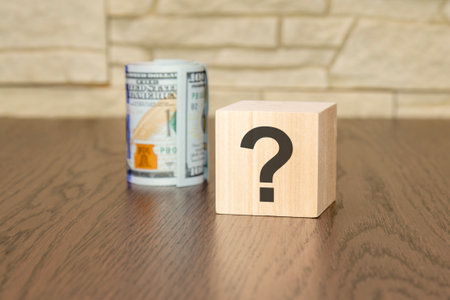 wooden cube with a question mark and dollar bills on a wooden tableの写真素材