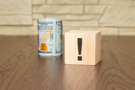 wooden cube with exclamation point and banknotes dollars on wooden tableの写真素材