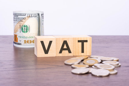top view of wooden blocks with text VAT (Value Added Tax) over US dollar banknotes on a brown background. TAX and VAT conceptの写真素材