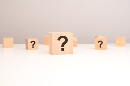 cube with question mark on wooden background, closeup. space for text