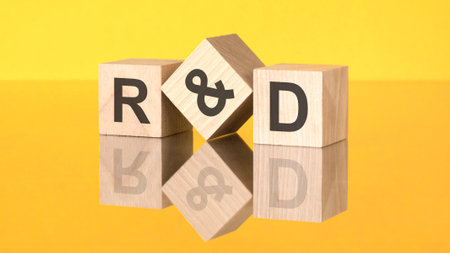 three wooden cubes with acronym R and D on yellow background. reflection of an image on a glass surface conceptの写真素材