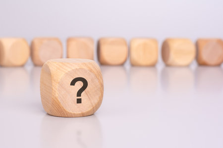 in the foreground is one wooden block with a question mark and a reflection from the table surface. in the background is a row of wooden blocks (out of focus).の写真素材