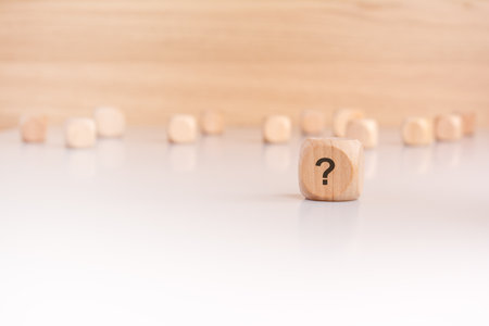 A wooden cube with a question mark written on it, placed prominently in the foreground. Numerous other wooden cubes are out of focus in the background, creating a sense of depth and curiosity.の写真素材