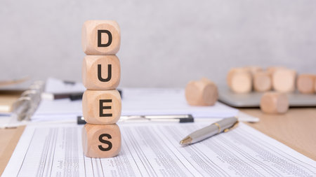 Wooden blocks spelling DUES on financial paperwork, illustrating accounting and dues tracking processesの写真素材