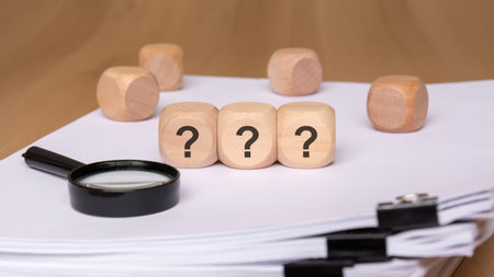 This artwork depicts uncertainty, featuring question marks on wooden cubes and various scattered documentsの写真素材